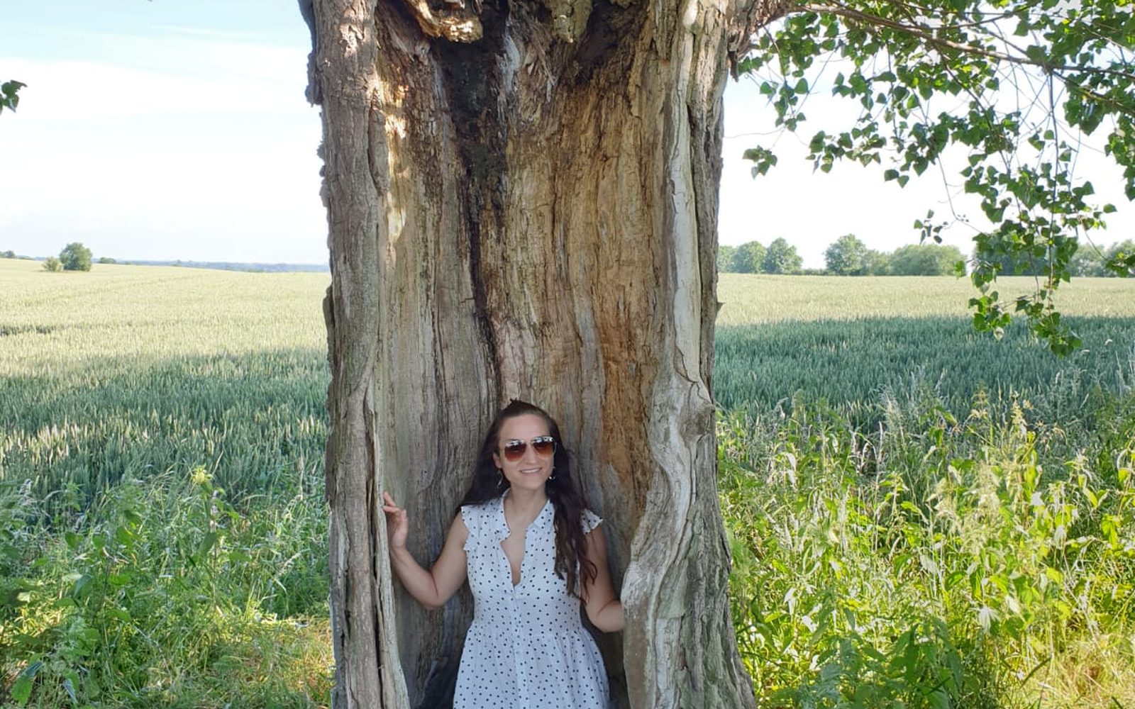 Nicole standing inside a hollow tree in a summer field