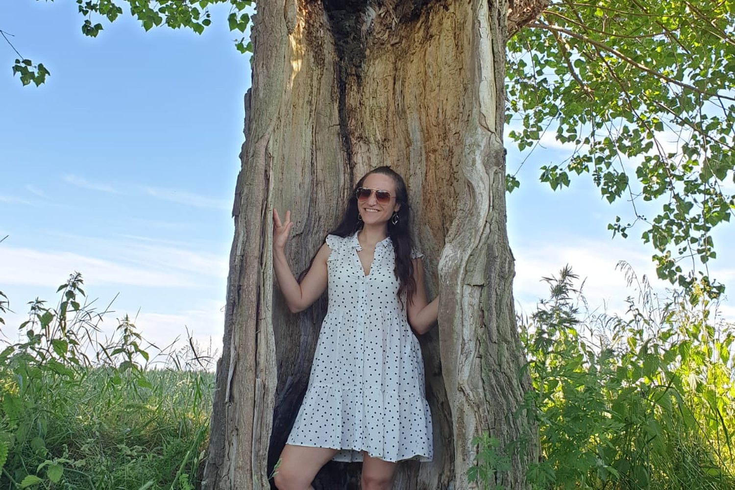 Nicole standing inside a hollow tree in a summer field